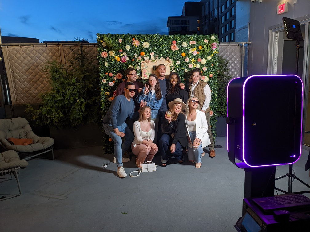 people posing in front of an open air photo booth with a flower greenery backdrop